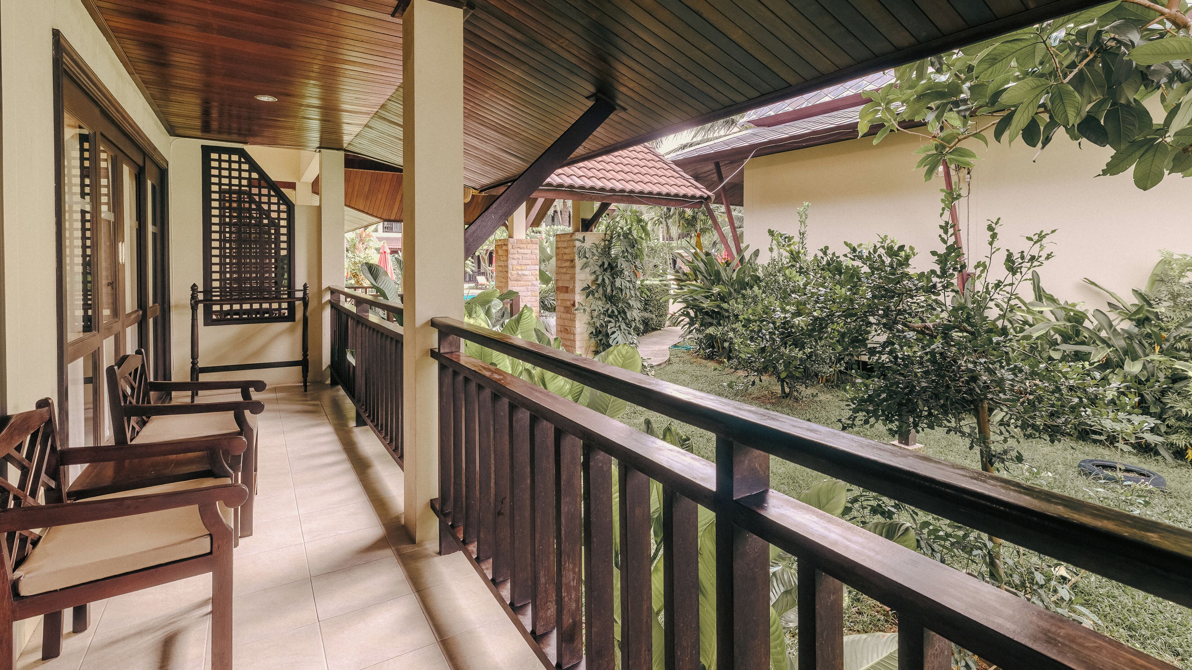 A balcony with wooden railings, a tiled floor, and a view of a garden with various plants.