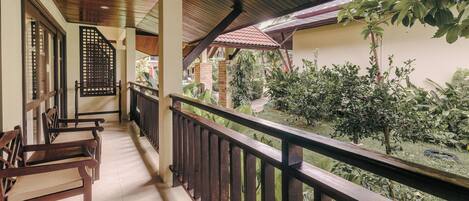 A balcony with wooden railings, a tiled floor, and a view of a garden with various plants.