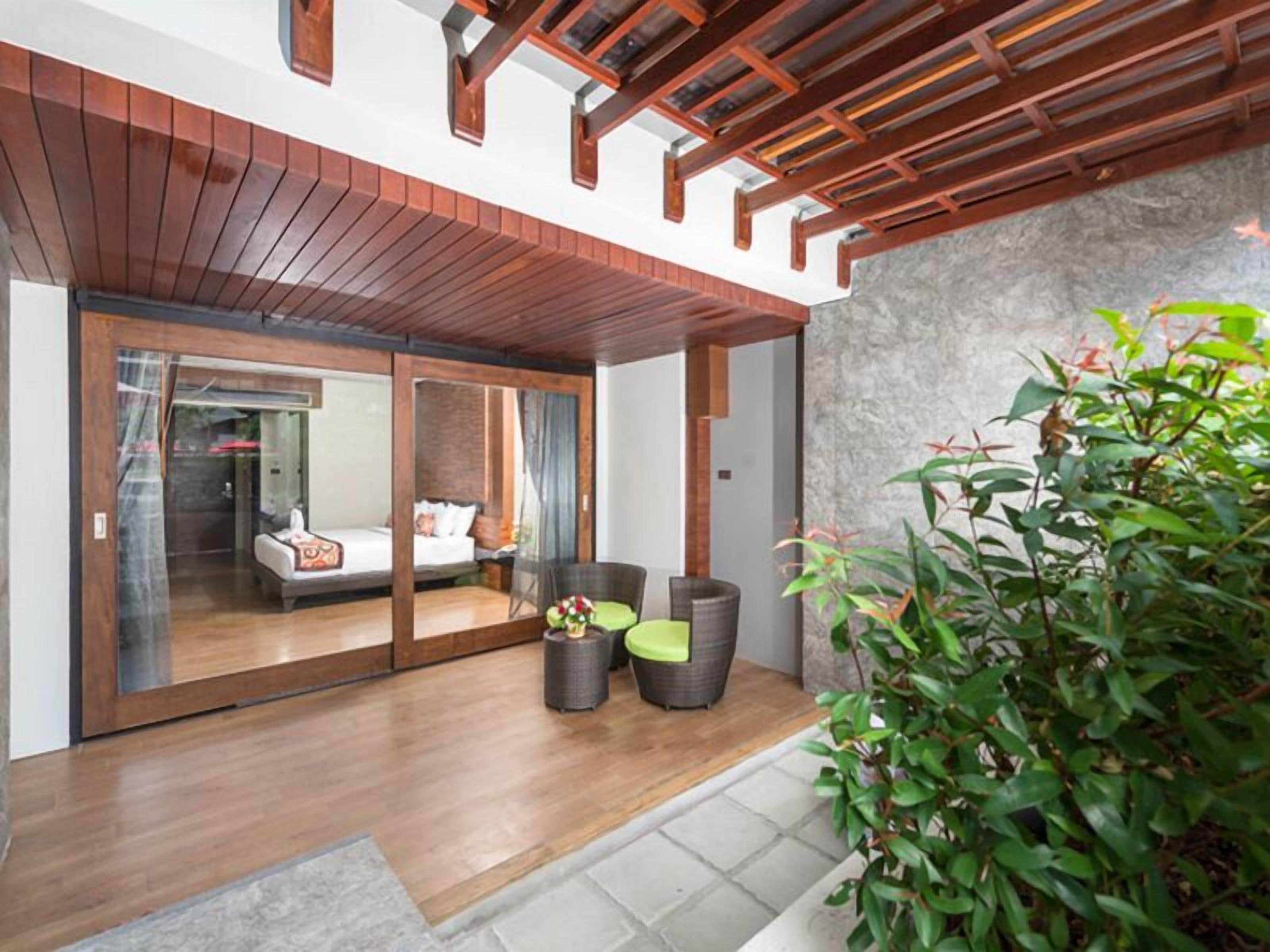 A modern hotel room with a wooden ceiling, a balcony with a sofa and chairs, and a view of the interior.