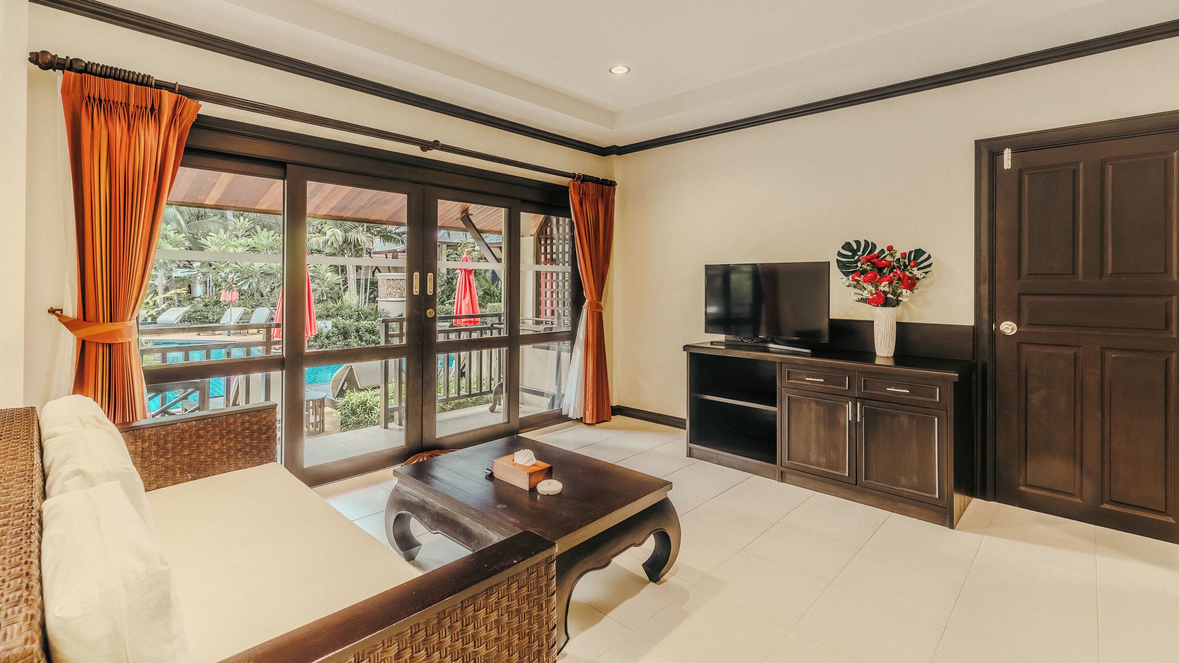 A living room with a sofa, coffee table, TV, and a view of a pool and greenery.