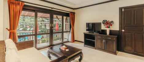 A living room with a sofa, coffee table, TV, and a view of a pool and greenery.