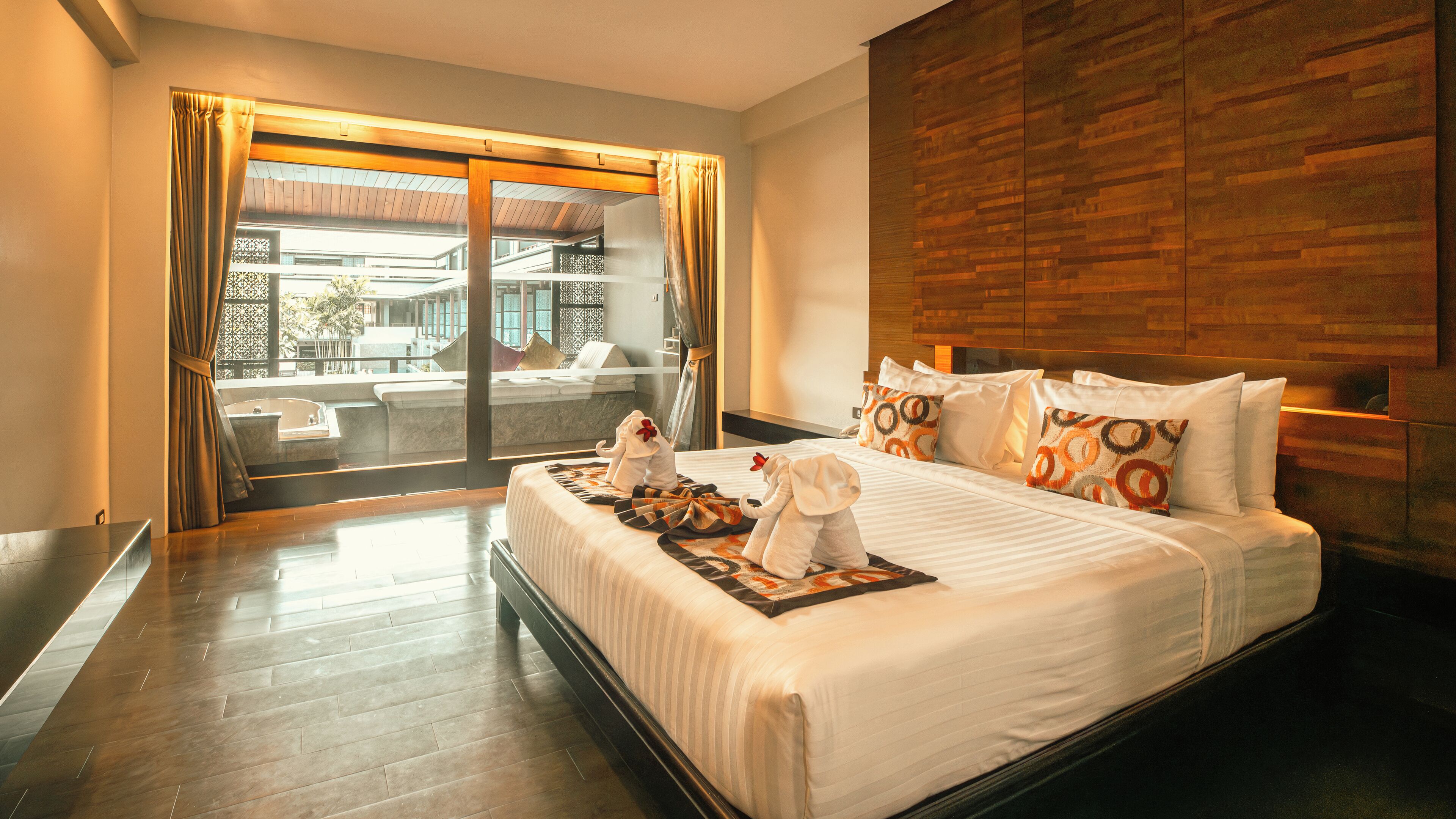 A hotel room with a large bed, wooden headboard, and a view of a pool and outdoor seating area.
