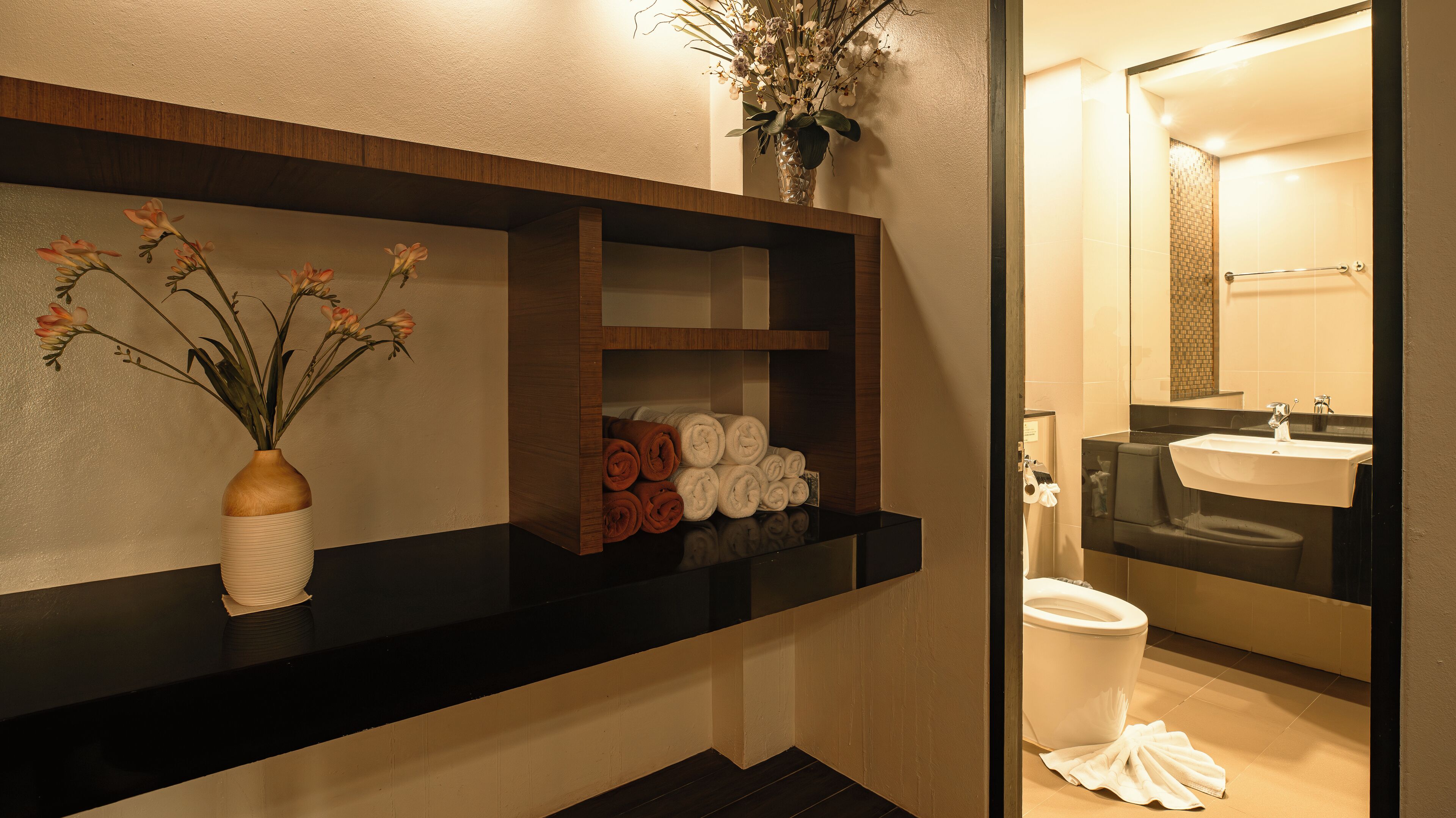 Un baño con encimera negra, un florero con flores y toallas dobladas con esmero.