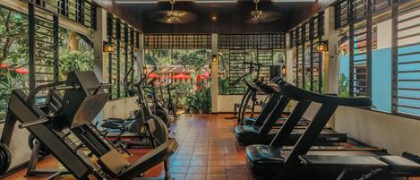 A gym with exercise equipment, wooden beams, and large windows overlooking a garden.