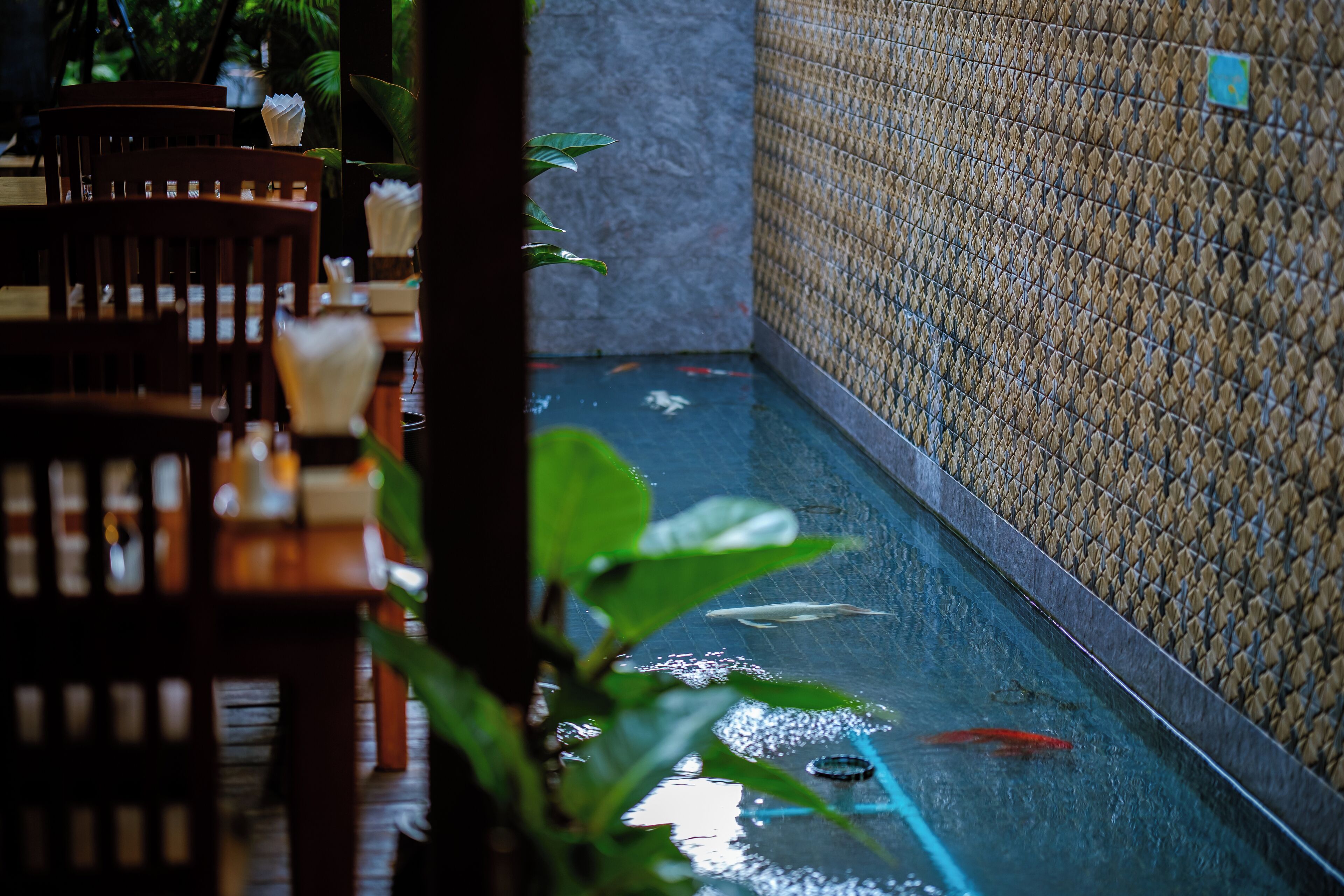 A narrow indoor water feature with a tiled wall and a wooden table with chairs.