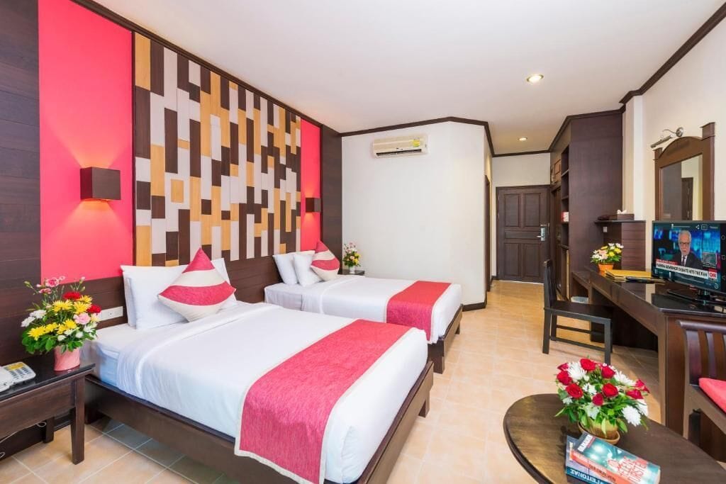 A hotel room with two beds, a TV, a desk, and a wall with a geometric pattern.