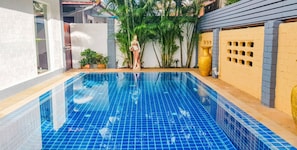 Una piscina con azulejos azules, rodeada de plantas en macetas y una pared amarilla con respiraderos.