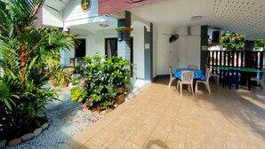 A covered patio with a tiled floor, a table with chairs, and a variety of potted plants.