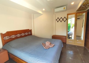 Una cama bien hecha con una colcha estampada, un cabecero de madera con diseño geométrico, una mesita de noche pequeña y un mueble espejo con puerta.