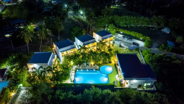 Um resort moderno com piscina central, vários quartos de hóspedes e paisagismo exuberante.