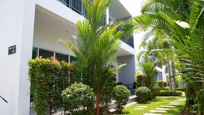 Um edifício moderno com fachada branca, varanda e um jardim bem cuidado com diversas plantas e um caminho de pedra.