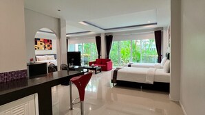 Quarto de hotel moderno com uma cama grande, uma cadeira vermelha, uma mesa de trabalho e vista para área verde lá fora.