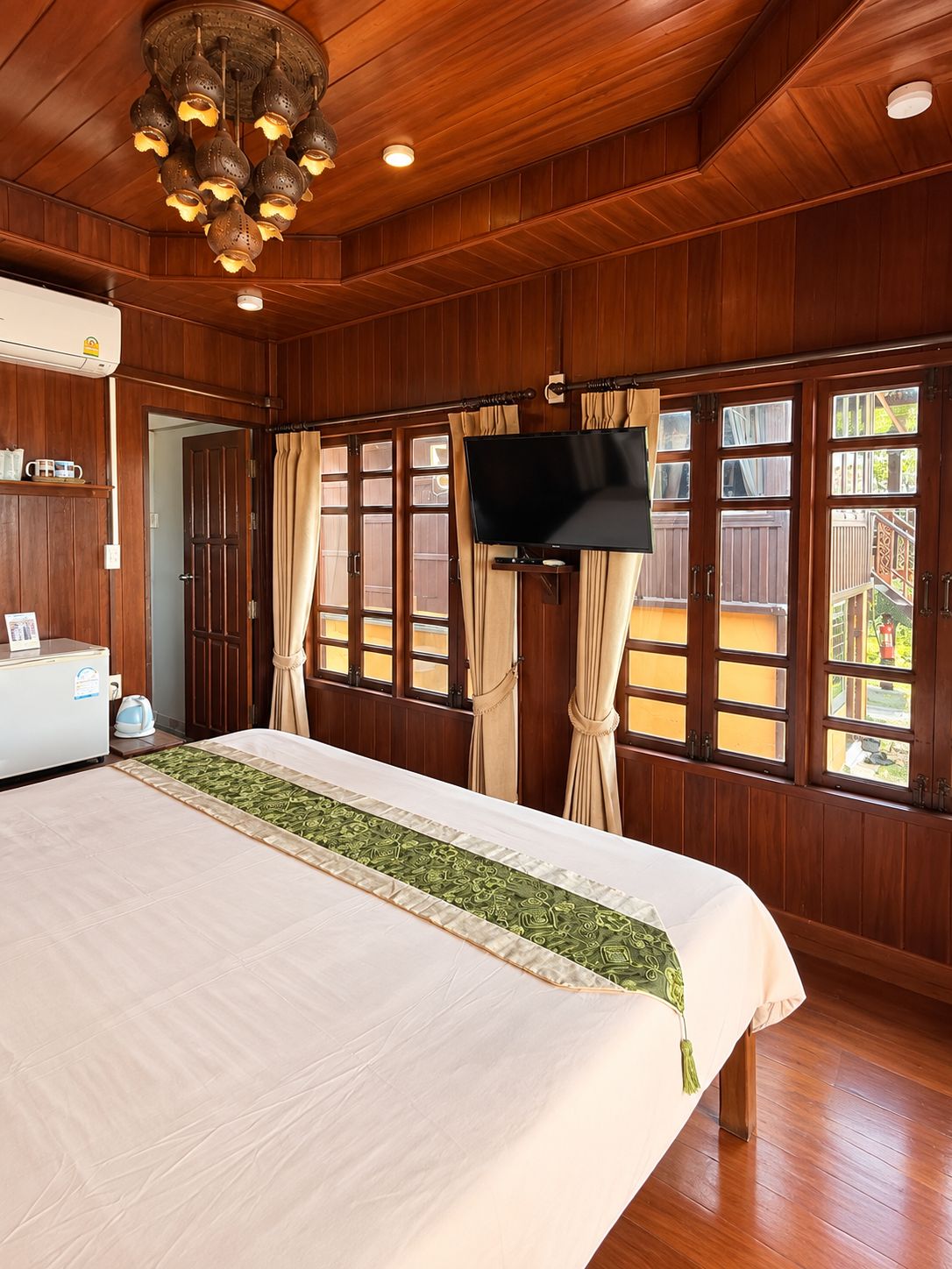 A hotel room with a large bed, wooden walls, a television, and a view of the outdoors.