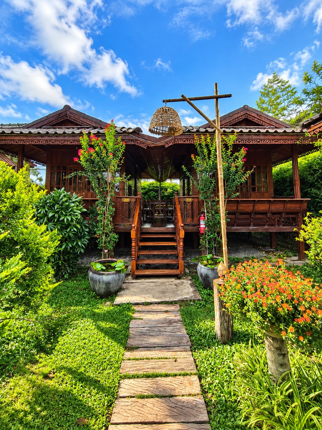 A traditional wooden house with a covered porch, a staircase leading to the entrance, and a garden with potted plants and a pathway.