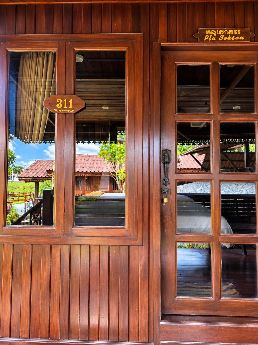 A wooden door with a number sign, a window, and a view of a building with a red roof.