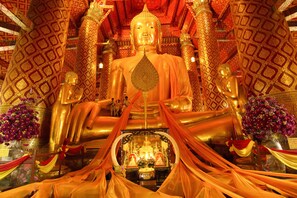 A large golden Buddha statue surrounded by intricate architectural details and floral arrangements. - Pludhaya Resort & Spa (Ayutthaya)