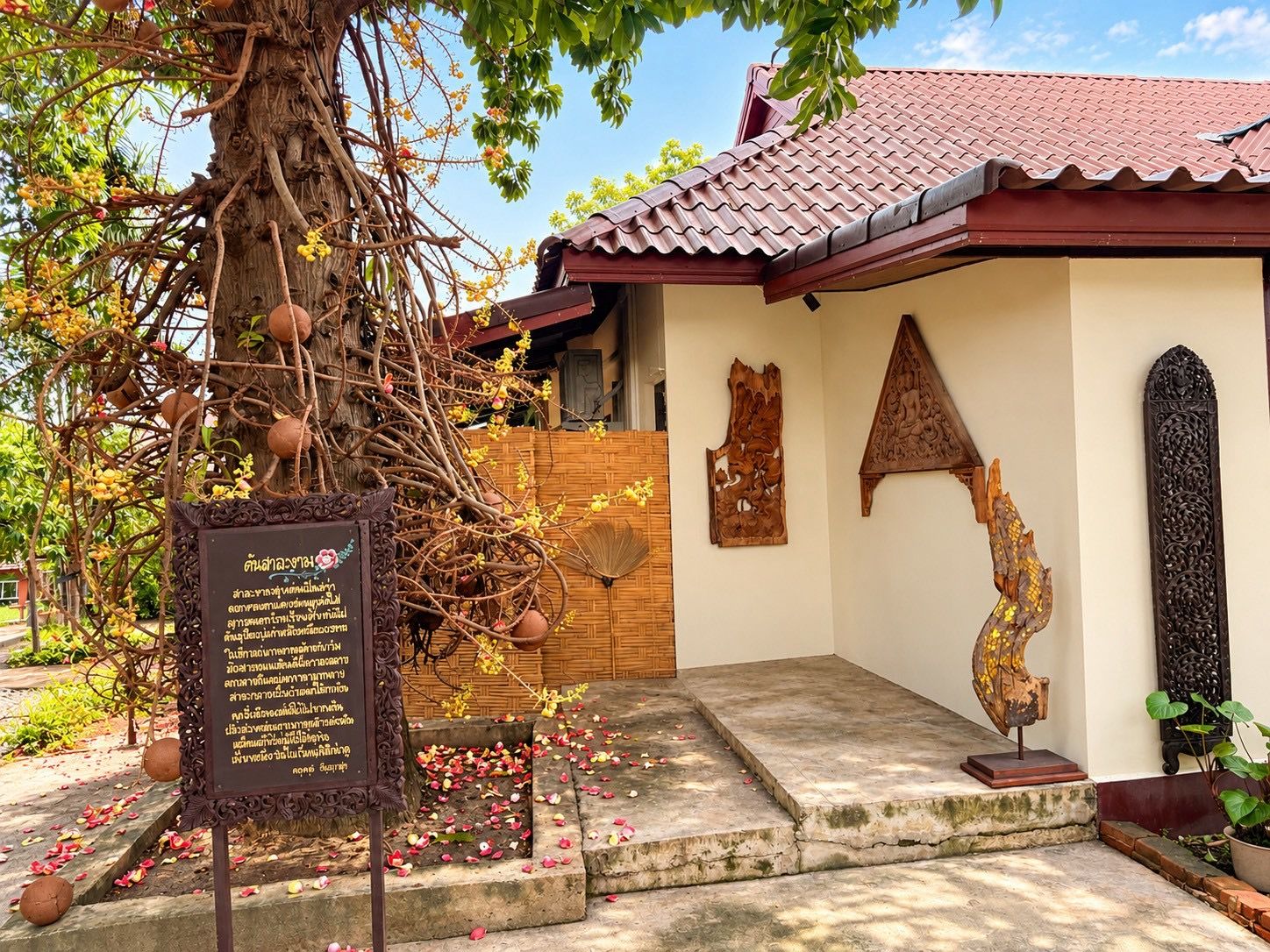 A traditional building with a tiled roof, a tree with yellow flowers, and a stone pathway leading to the entrance.
