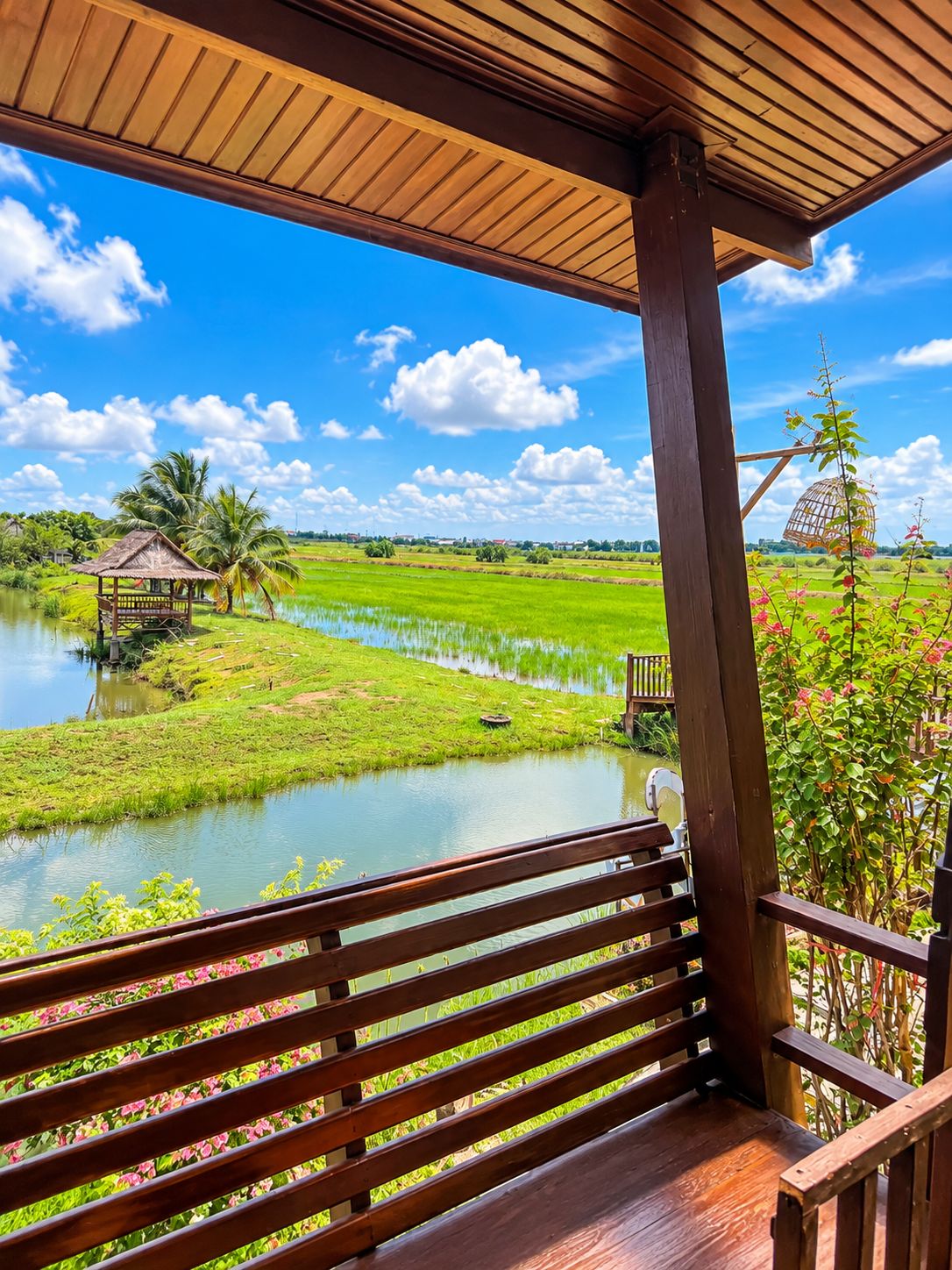 Una terraza de madera con un banco que da a un paisaje verde exuberante con un cuerpo de agua y una pequeña construcción.