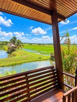 Una terraza de madera con un banco que da a un paisaje verde exuberante con un cuerpo de agua y una pequeña construcción.