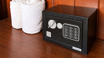 A black safe with a keypad and a small logo, next to a pair of white towels on a wooden surface.