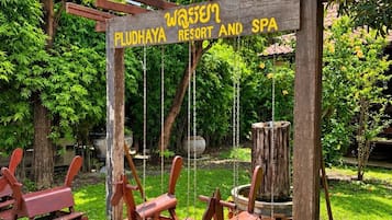 A wooden sign with 'PLUDHAYA RESORT AND SPA' written on it, surrounded by greenery and a swing set.