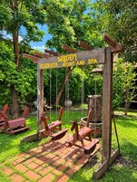 Un letrero de madera con la inscripción 'PLUDHAYA RESORT AND SPA', rodeado de follaje y un columpio.