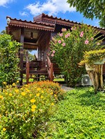 Una estructura de madera con balcón, rodeada de abundante vegetación y plantas en flor.