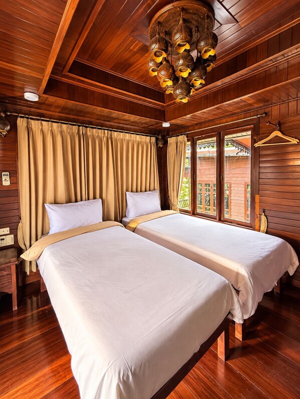 A wooden room with two beds, a chandelier, and curtains.