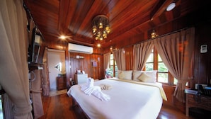Una cama grande con sábanas blancas, techo de madera y ventana con cortinas.