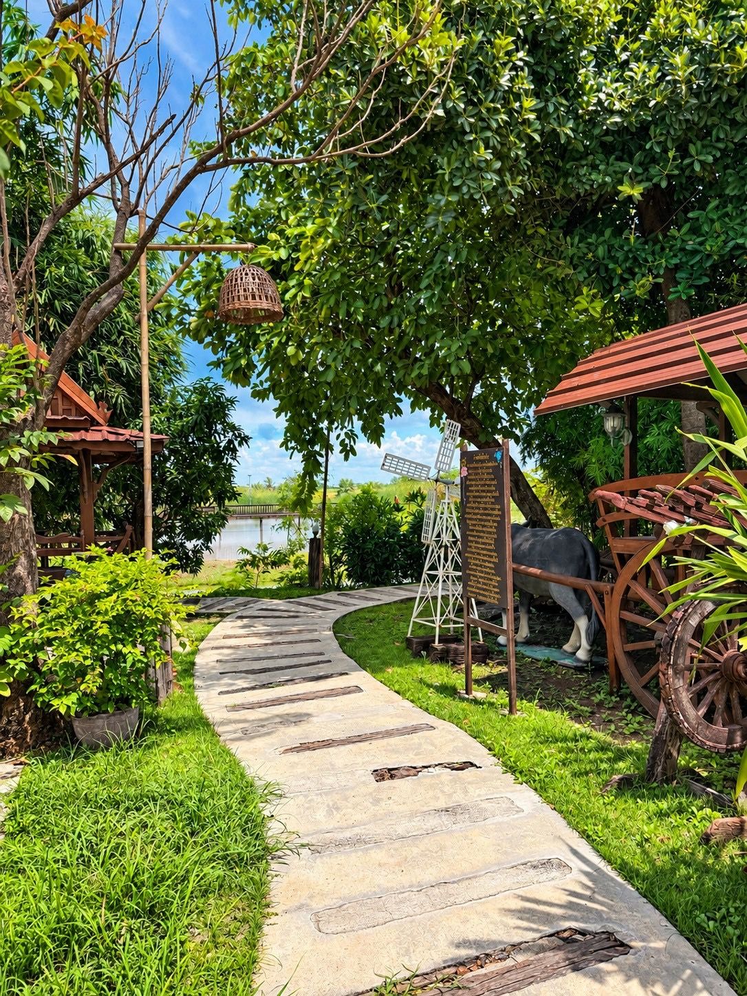 A garden pathway with a rustic wooden structure, a metal sign, and a decorative cart.