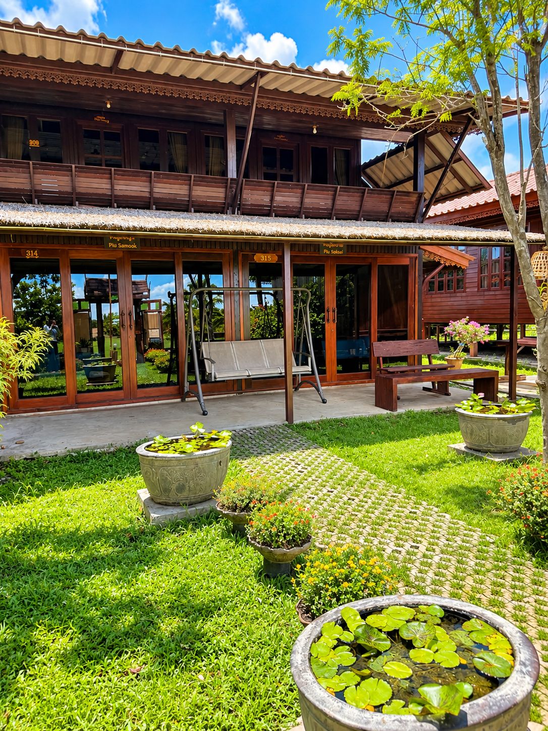 A wooden building with a covered patio area, outdoor seating, and a garden with potted plants and a pond.