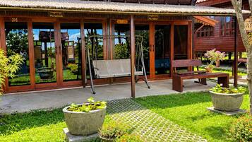 A wooden building with a covered patio area, outdoor seating, and a garden with potted plants and a pond.