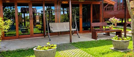 A wooden building with a covered patio area, outdoor seating, and a garden with potted plants and a pond.