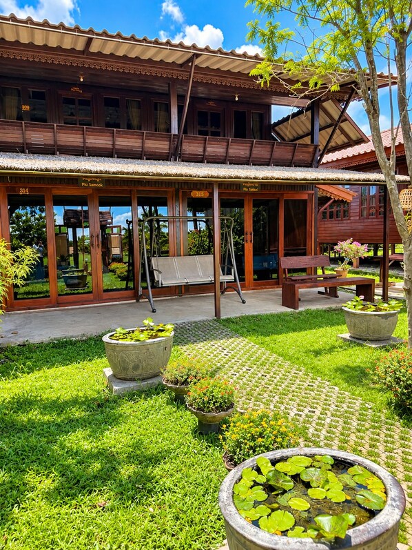 A wooden building with a covered patio area, outdoor seating, and a garden with potted plants and a pond.