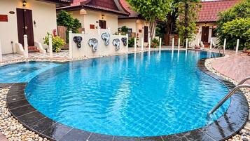 A swimming pool with a curved edge, surrounded by a pebble border, and adjacent to a building with a red-tiled roof.