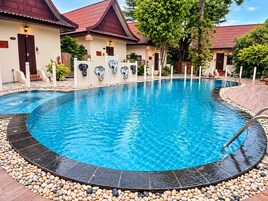 Una piscina de borde curvo, rodeada por un borde de piedras y contigua a un edificio con techo de tejas rojas.