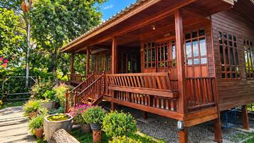 A wooden house with a porch, potted plants, and a stone pathway.