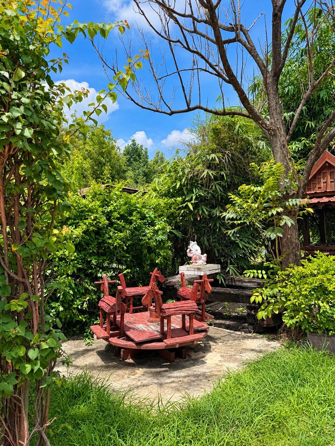 A garden with a wooden bench area, surrounded by lush greenery and trees.