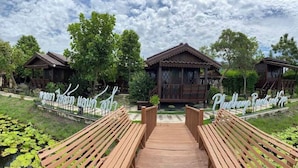 Un sendero de madera conduce a una hilera de cabañas de estilo tradicional, con un estanque y vegetación en primer plano.
