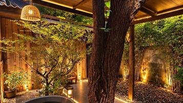 A tranquil outdoor area with a wooden pergola, a large planter with a tree, and a water feature.