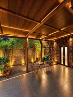 Un patio al aire libre con techo de madera, paredes de piedra y una zona de estar con mesas y sillas.