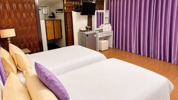 Ein Hotelzimmer mit zwei Betten, einem Fernseher, einem Schreibtisch mit Spiegel und violetten Vorhängen.