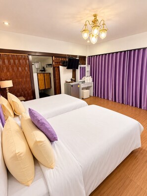 A hotel room with two beds, a television, a desk with a mirror, and purple curtains.