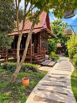 A traditional wooden building with a tiled roof, surrounded by lush greenery and a stone pathway.