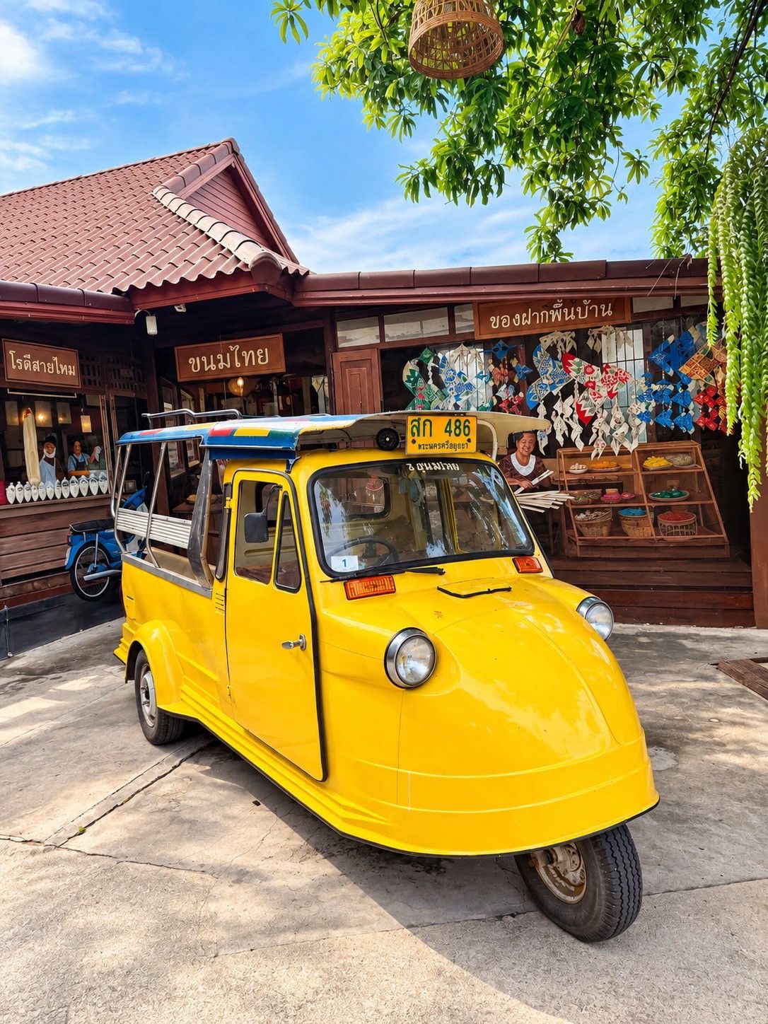 A yellow tuk-tuk parked in front of a building with a red roof and a sign with Thai script.