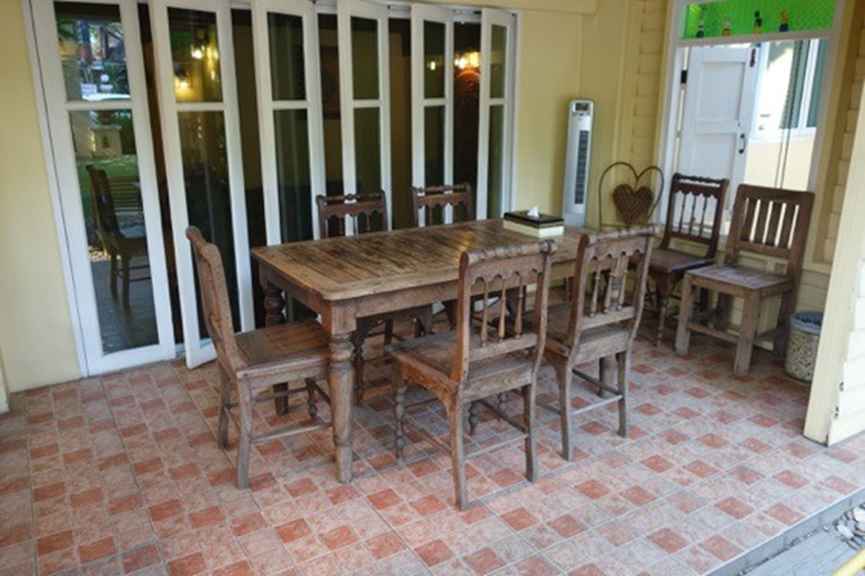 A wooden dining table with six chairs, a tiled floor, and a sliding glass door in the background.