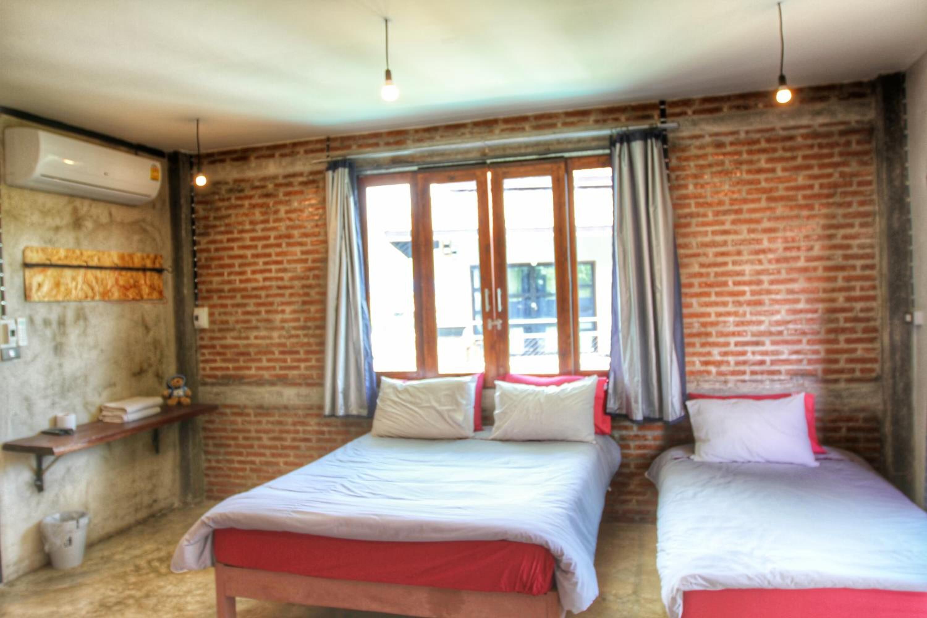 A room with two beds, a brick wall, a window with curtains, and a hanging light fixture.
