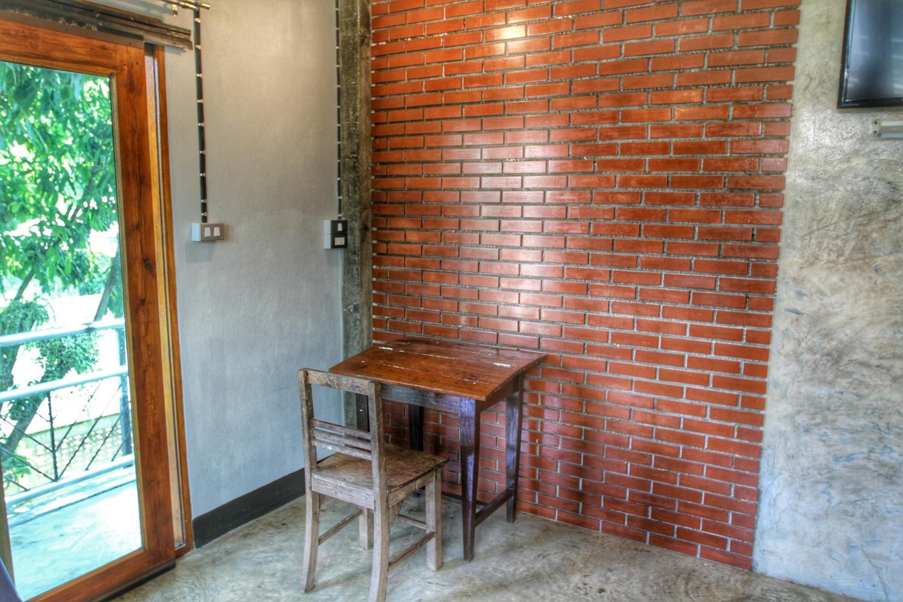 A corner room with a brick wall, a wooden table, and a chair.