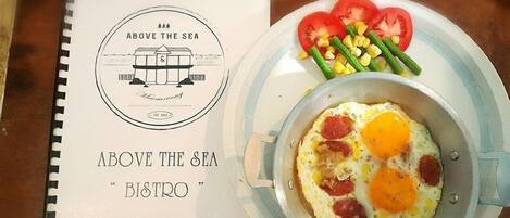 A menu titled "Above the Sea Bistro" with a breakfast dish of eggs, tomatoes, and corn.