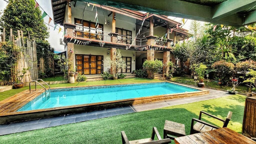 Une maison à deux étages avec une piscine, du mobilier d’extérieur et une végétation luxuriante.
